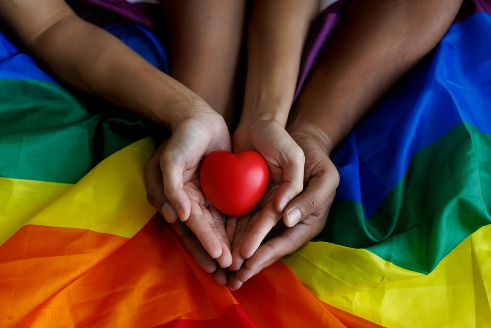 couple holding a heart in hand on LGBT flag background