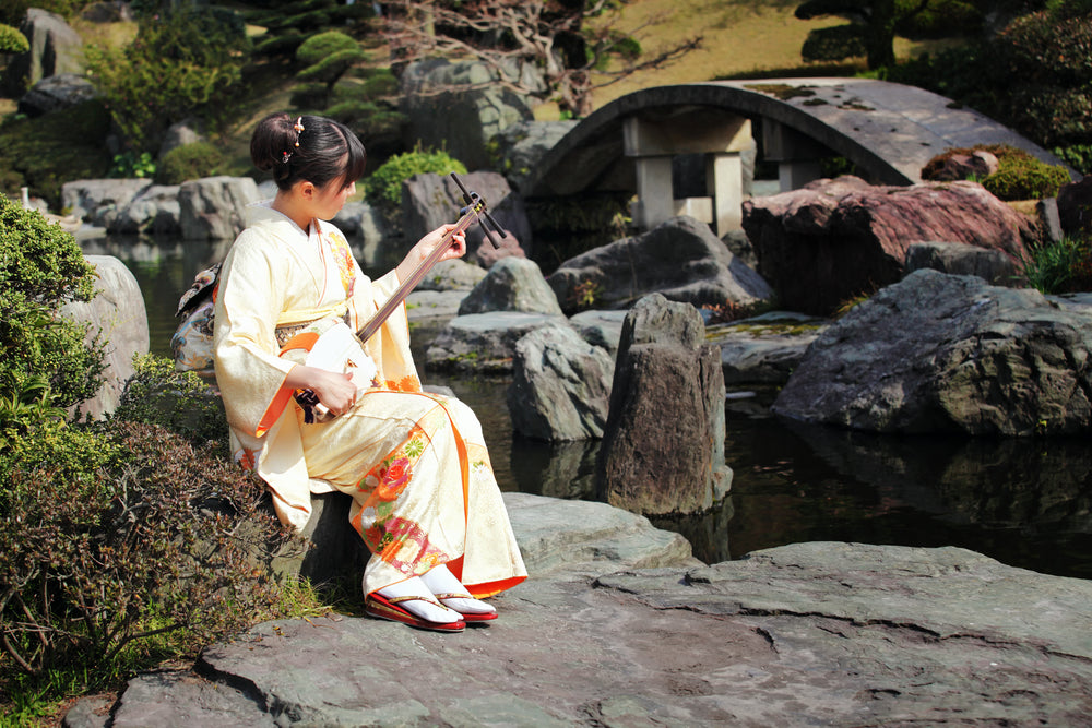 Woman playing shamisen (traditional Japanese guitar) in Japanese garden