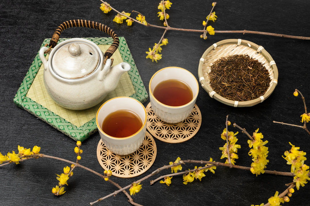 A teapot along with two tea cups filled with Japanese hojicha roasted green tea and a bowl of hojicha leaves.