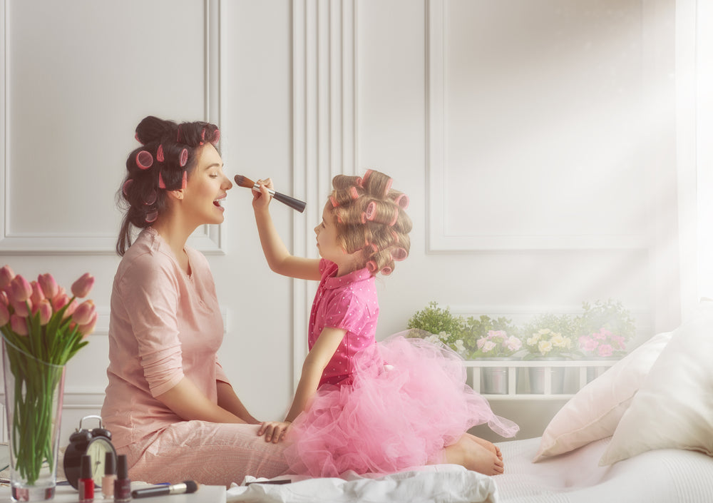 Happy loving family. Mother and daughter are doing hair and having fun. Mother and daughter doing your makeup sitting on the bed in the bedroom.